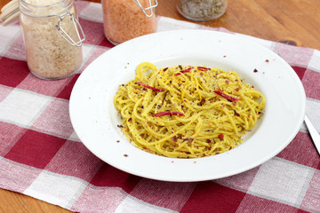 Spaghetti with pesto, chili flakes and chili on a white plate.