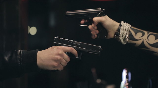 Two male hands with guns take aim at each other. Close up