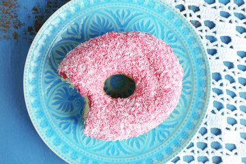 Bitten delicious donut on plate on wooden table close-up