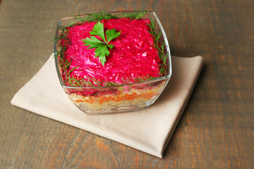 Russian herring salad in glass bowl on wooden table background