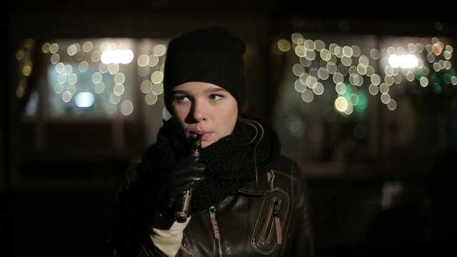 Teenager girl in the evening smoking electronic cigarette.