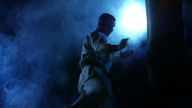 Silhouette karate man practicing on the sandbag on blue