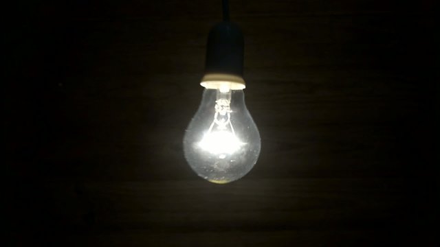 Lit bulb swinging back and forth in front of a wooden board