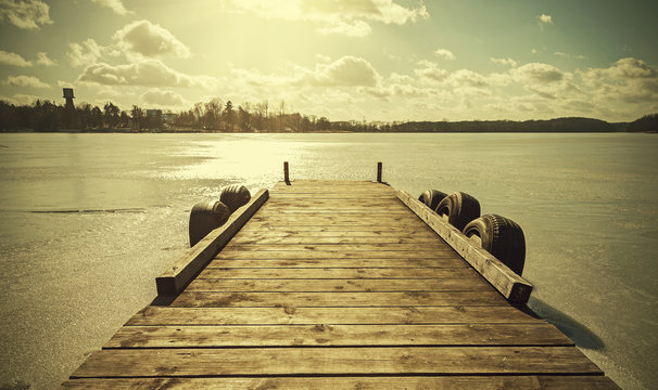 Vintage retro toned image of a pier on frozen lake.