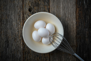 Eggs in a Bowl with a Whisk on Rustic Wood Background