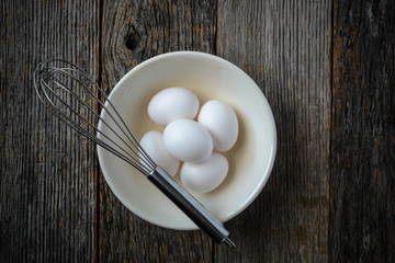 Eggs in a Bowl with a Whisk on Rustic Wood Background