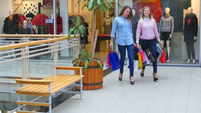 Two beautiful girls with shopping bags goes on shopping center
