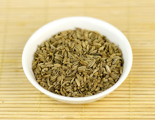 Cumin seeds in bowl against wooden background