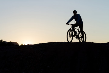 Silhouette of a cyclist with sunset on the top of a hill