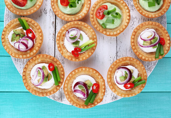 Tartlets with greens and vegetables with sauce on tray on table