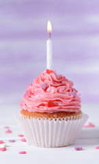 Delicious birthday cupcake on table on light purple background