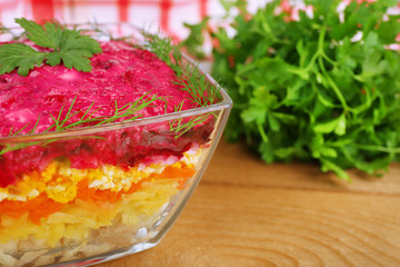 Russian herring salad in glass bowl on wooden table background