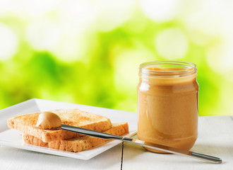 Jar of peanut butter and toasts on nature background