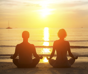 Young yoga couple meditating during amazing sunset on the beach.