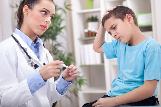 female doctor measuring temperature of boy in clinic