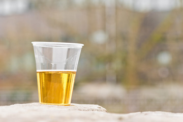 Ein Becher - halb voll mit Bier - steht auf einer Mauer