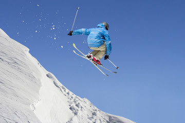 Jumping freestyle skier through air on blue sky background