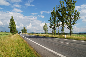 Fototapeta premium Empty road lined with poplar alley, coming from afar white truck