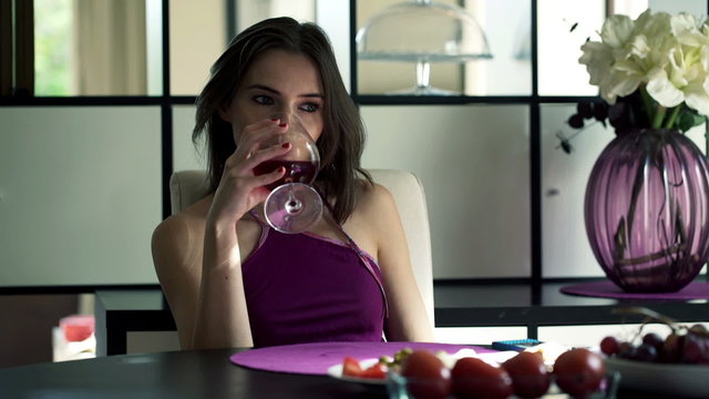 Sad, thoughtful woman drinking wine by the table at home