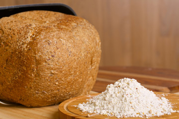 Fresh loaf of rye bread and some flour on wooden table