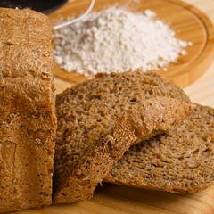 Fresh cutted loaf of rye bread and some flour on wooden table