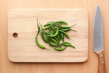 A pile of green chilli peppers on wooden chopping board
