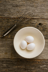 Eggs in a Bowl with a Whisk on Rustic Wood Background