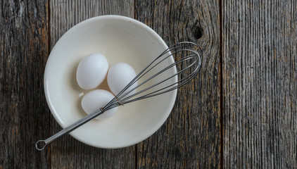 Eggs in a Bowl with a Whisk on Rustic Wood Background