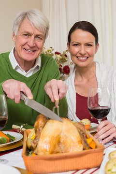 Grandfather carving chicken while woman drinking red wine