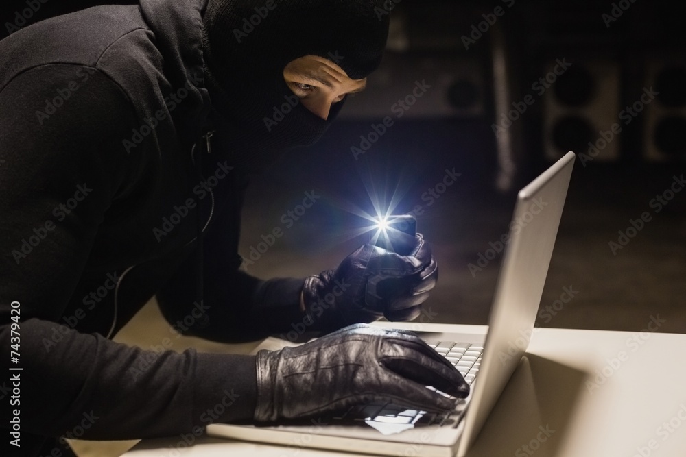 Poster robber hacking a laptop while making light with his phone