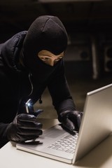 Robber hacking a laptop while making light with his phone