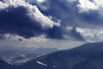 Helicopter in winter mountains and cloudy sky