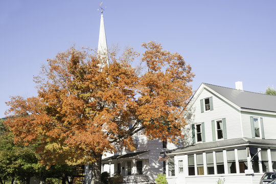 White traditional church with tree in full fall color.