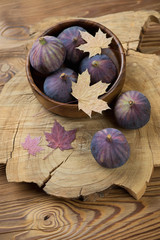 Wooden bowl with ripe fig fruits and maple leaves, vertical shot
