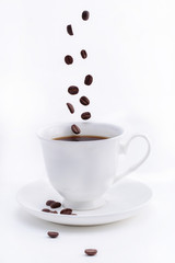 Drop in a cup of coffee beans isolated on white.