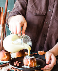 Cinnabon cinnamon rolls with cream sauce to pour, hands