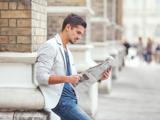 Young businessman reading newspaper outdoors