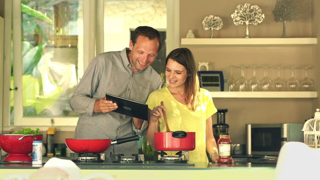 Happy couple using tablet computer and cooking in kitchen