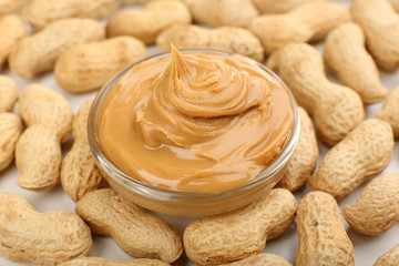 Creamy peanut butter in bowl on peanut background, close-up