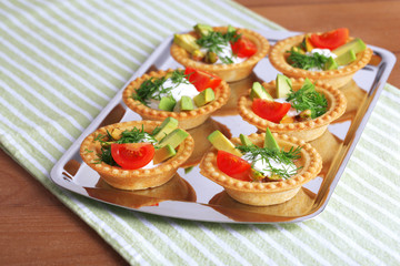 Tartlets with greens and vegetables with sauce on tray on table