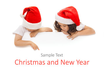 Happy little kids in Santa hat peeking from behind blank sign