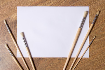 paint brushes and blank white paper on wooden background