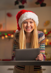 Portrait of happy teenager girl in santa hat using tablet pc