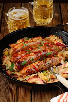 Sausages fried in cast iron skillet with two beer mugs