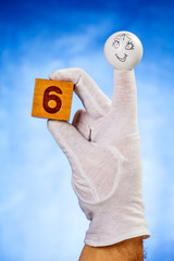 Number six on wooden cube hold by finger puppet