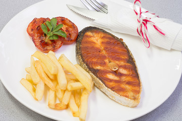 Salmon steak served with chips and grilled tomatos