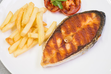 Salmon steak served with chips and grilled tomatos