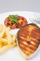 Salmon steak served with chips and grilled tomatos