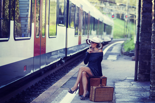 A woman sitting on a suitcase is waiting for the train at the station. Romantic and sweet scene. The woman is alone and feels strong