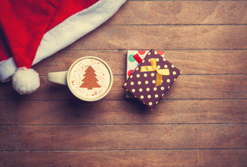 Cappuccino with christmas hat and gift on wooden table.